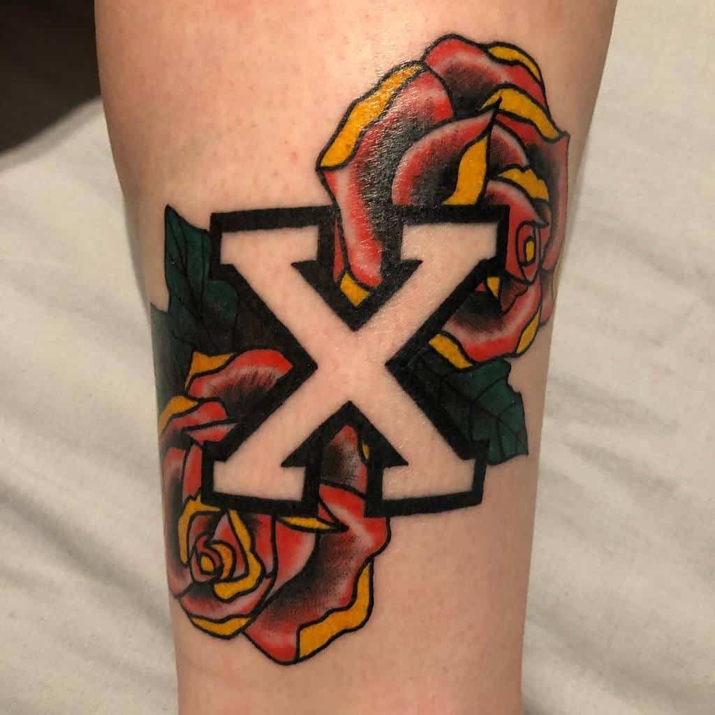 Straight edge tattoo with a bold black-outlined 'X' surrounded by vibrant red and yellow roses with deep green leaves