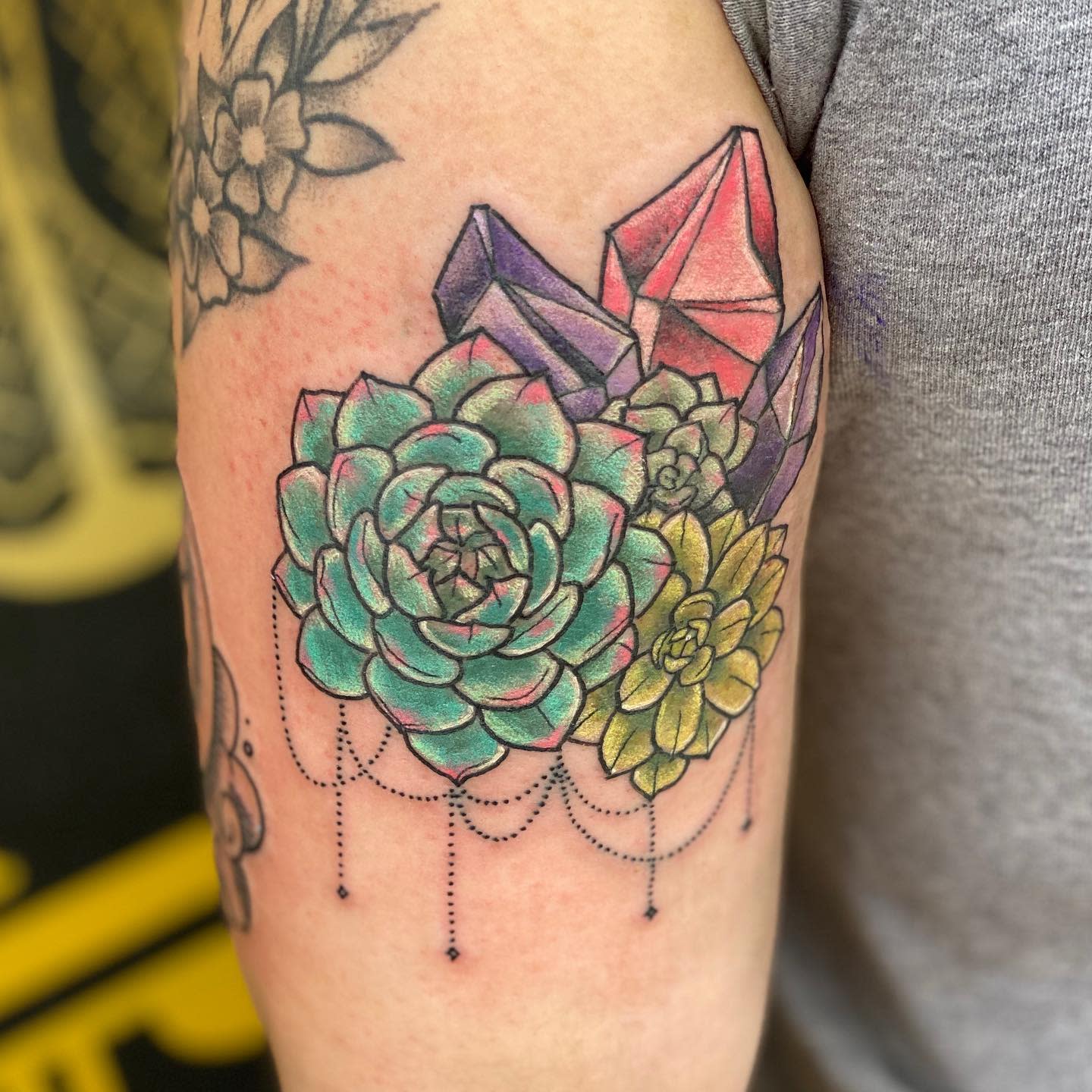 Tattoo of succulents and crystals on the upper arm with dotwork details in the background