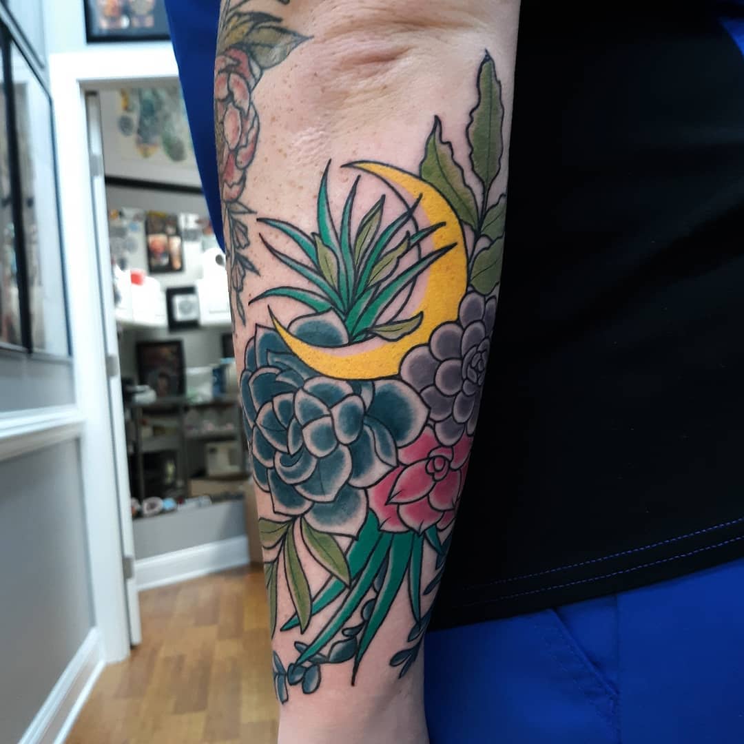 A forearm tattoo with a yellow crescent moon and different succulents
