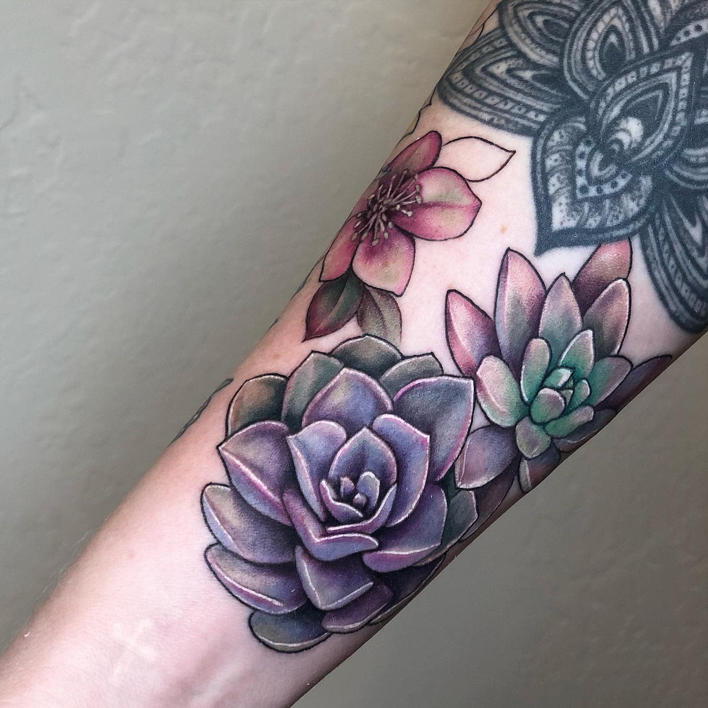 Forearm tattoo featuring colorful succulents and a flower with mandala design above