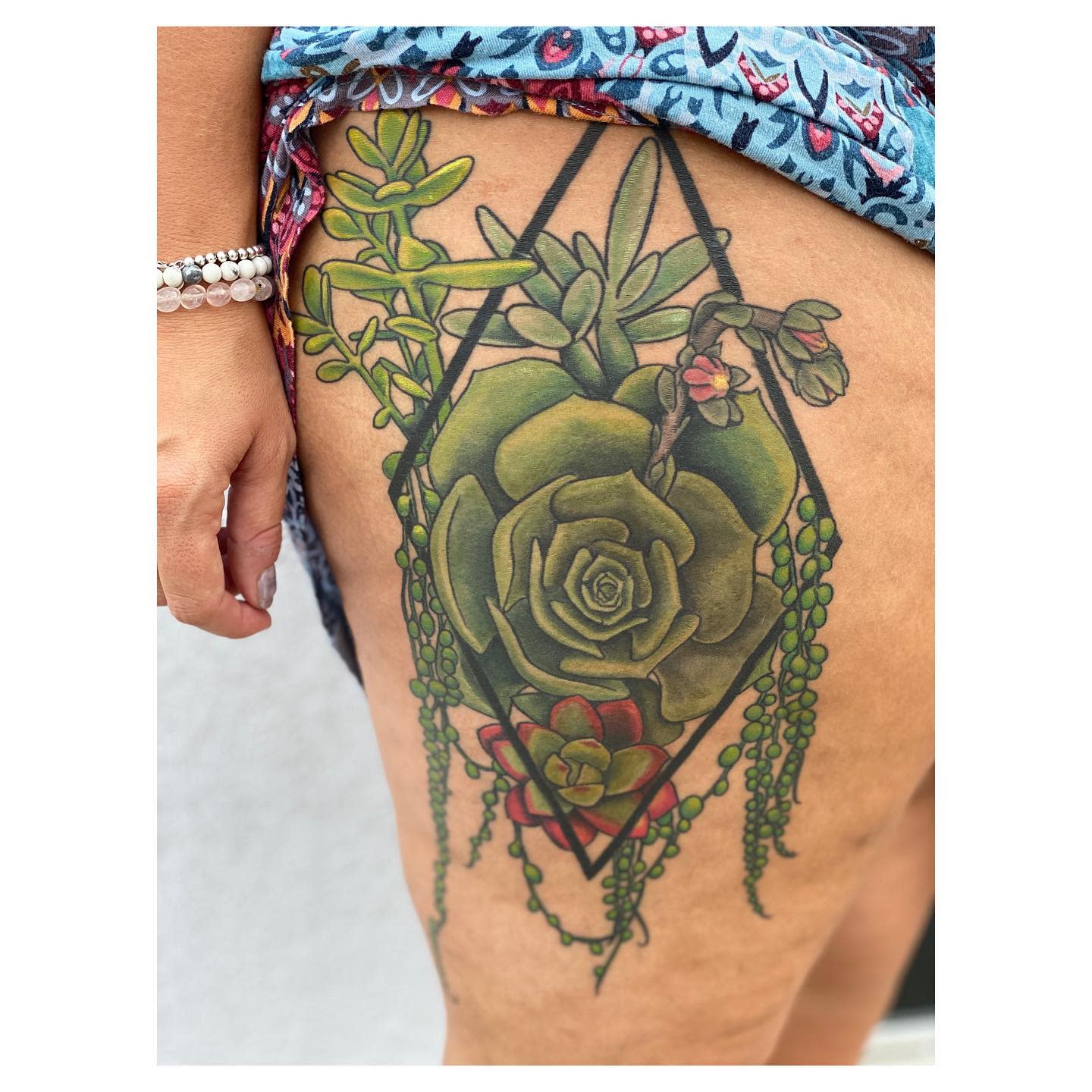 Thigh tattoo featuring various green succulents and flowers inside a geometric diamond shape
