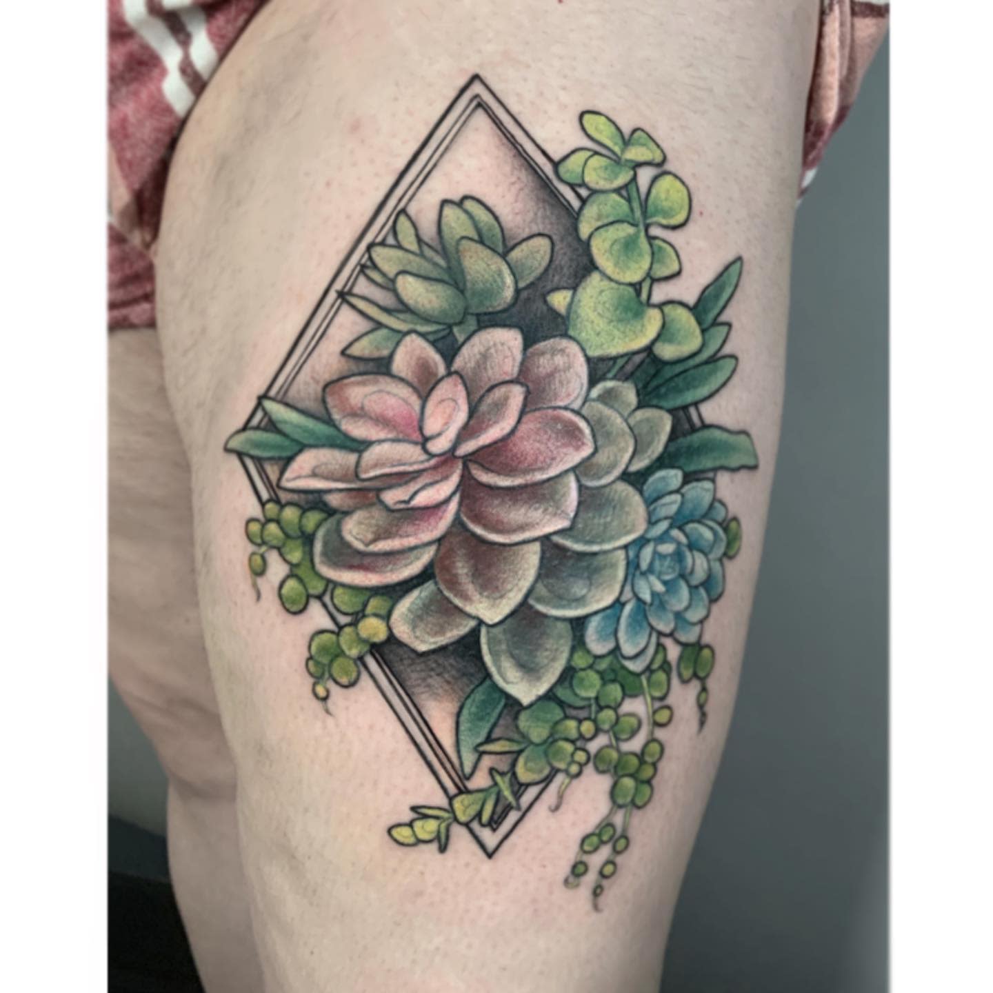 Tattoo of colorful succulents inside a diamond frame on an upper thigh