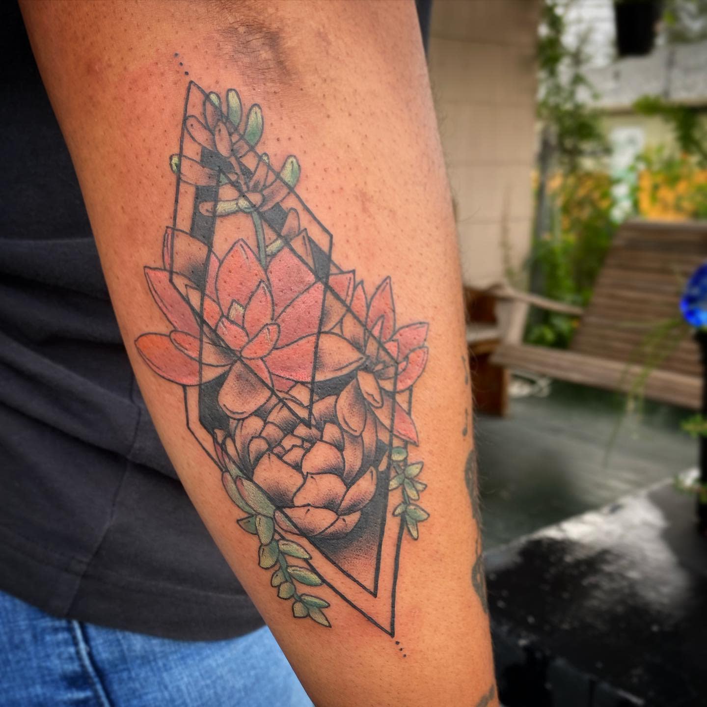 Tattoo of geometric shapes with colorful flowers and succulents on a forearm