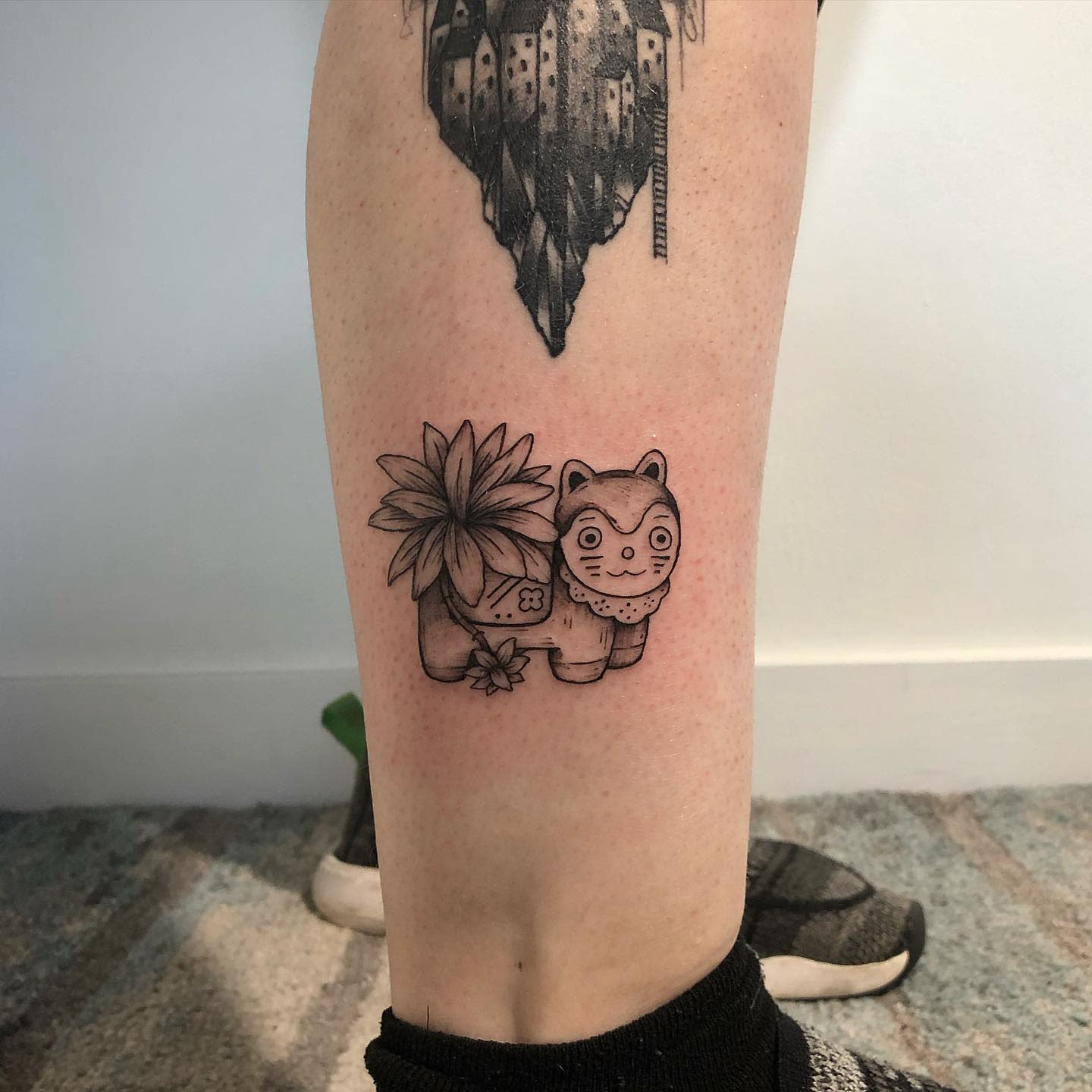 Black and white leg tattoo of a cat-plant hybrid with flowers on a calf