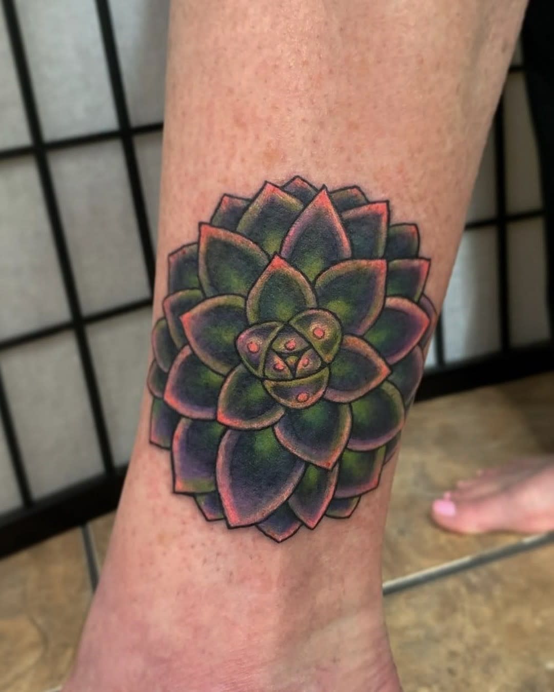 A vibrantly colored succulent tattoo on the inside of someone's ankle