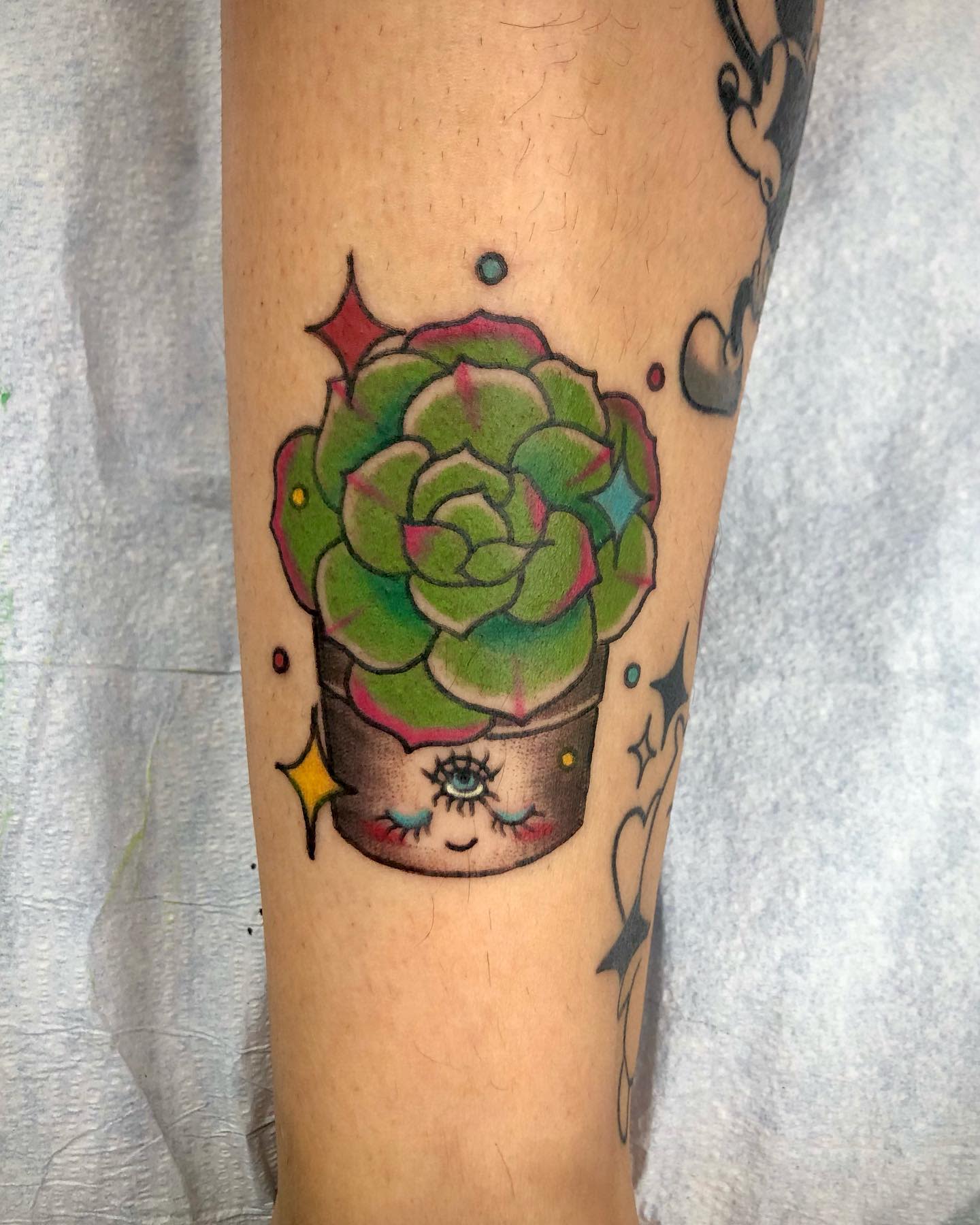 Tattoo of a smiling succulent in a pot with colorful stars around it on a forearm