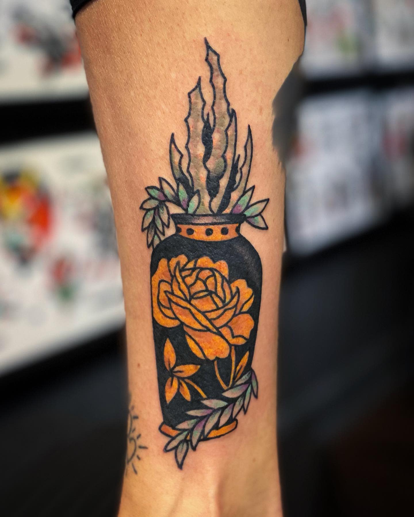 Tattoo of a yellow rose in a black vase with succulents on arm