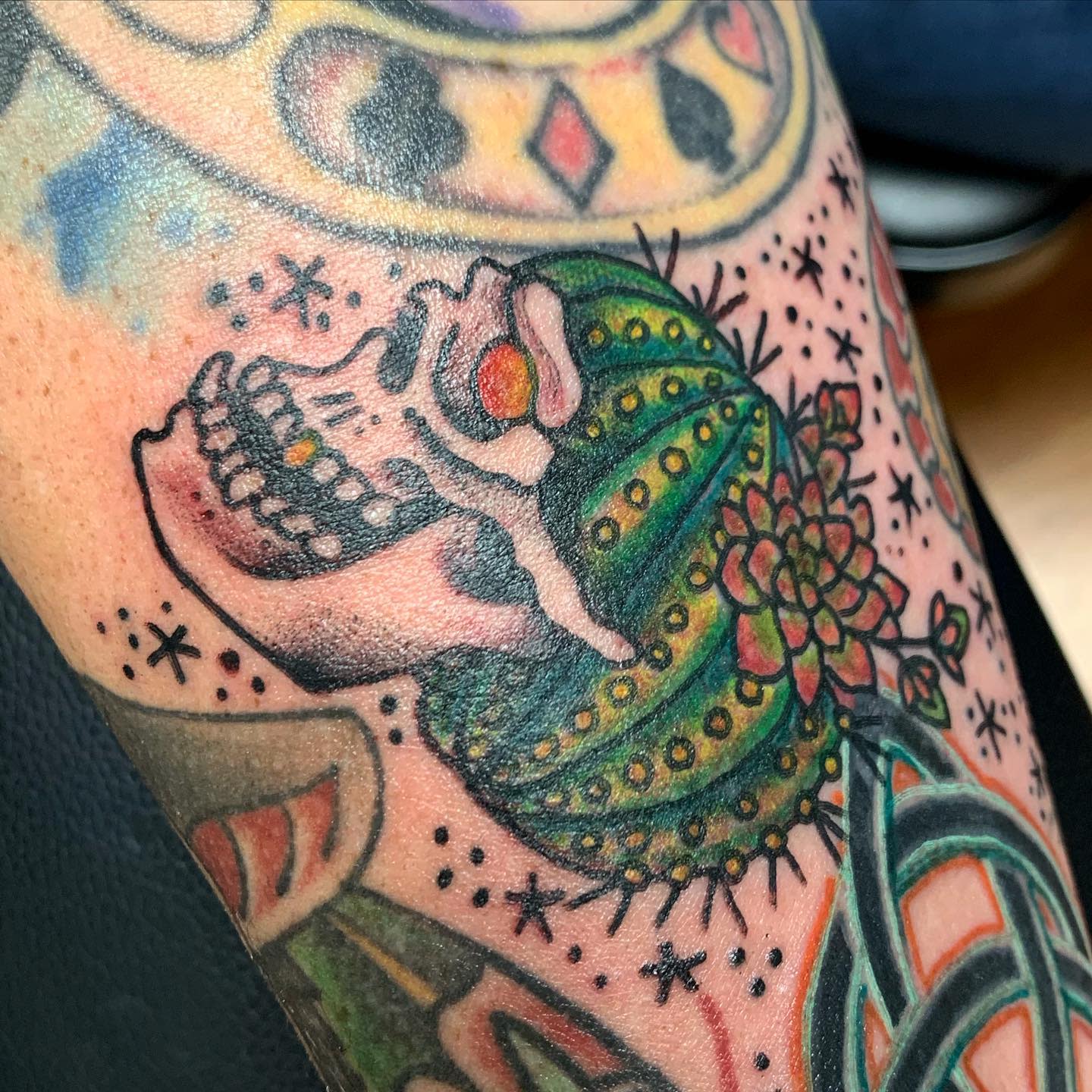 Tattoo of a skull merged with a green cactus blooming with red flowers on a tattooed arm