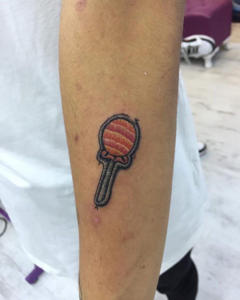 Small embroidery-style tattoo of a swirled lollipop with detailed stitching effects and a vintage patchwork look.