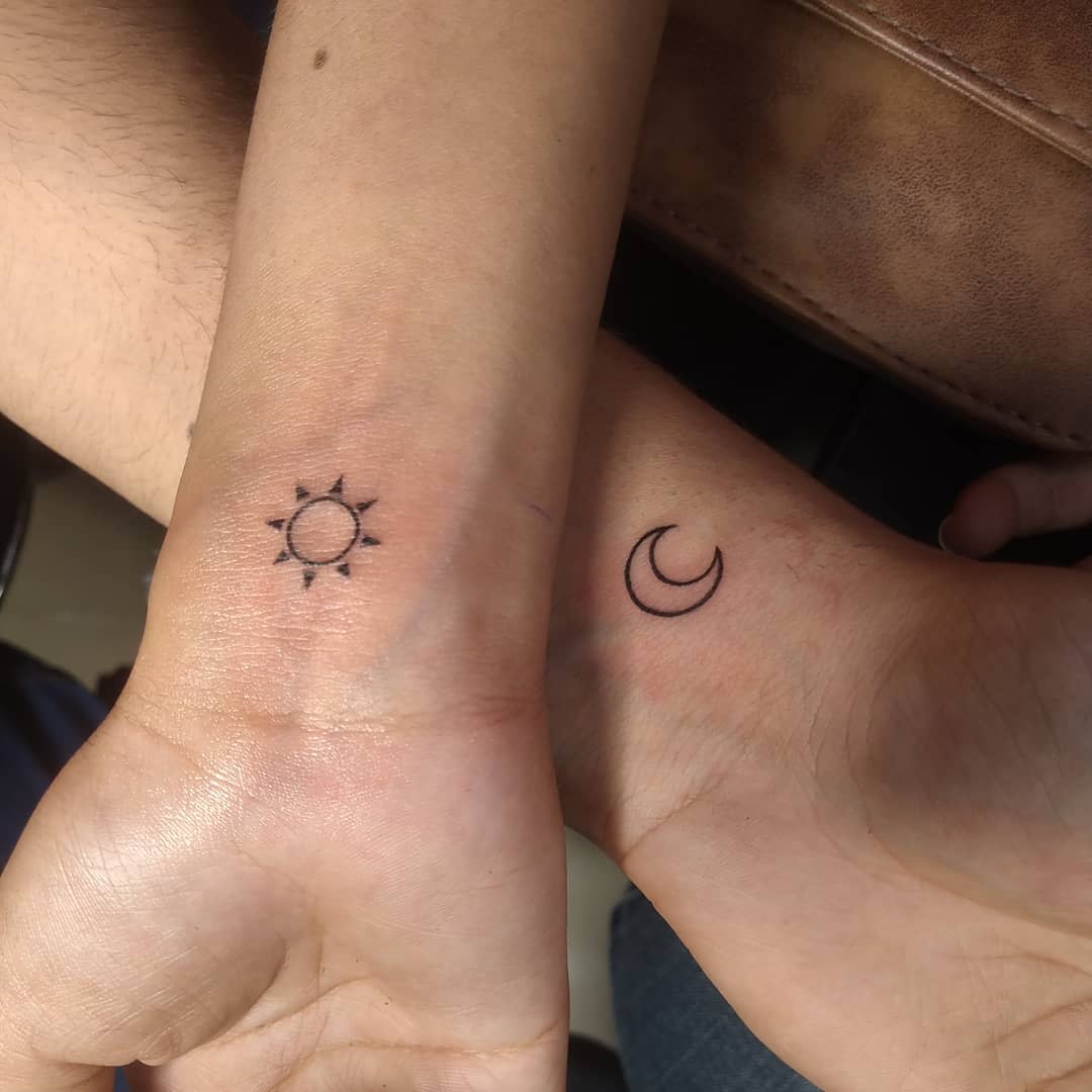 Tattoo of a sun on one wrist and a crescent moon on the other