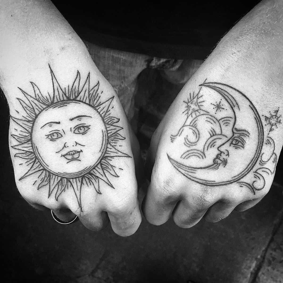 Black and white tattoos of a sun on one hand and a crescent moon on the other hand