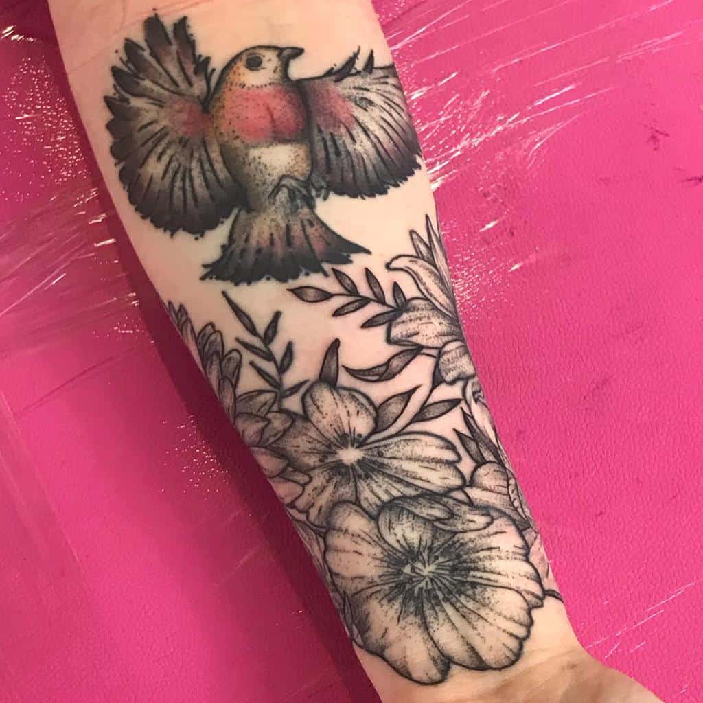 Forearm tattoo of a bird above detailed flowers