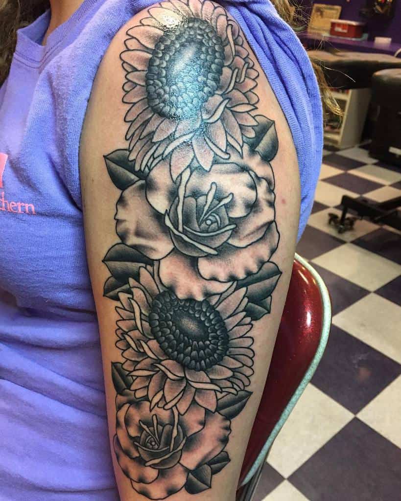 Black and gray tattoo of sunflowers and roses on an upper arm