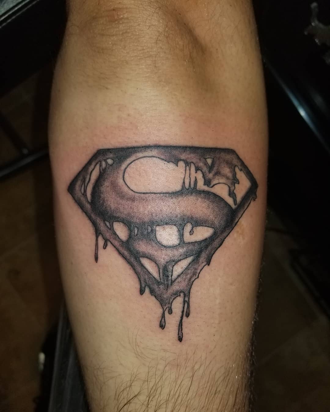 A tattoo of a melting Superman logo on a leg