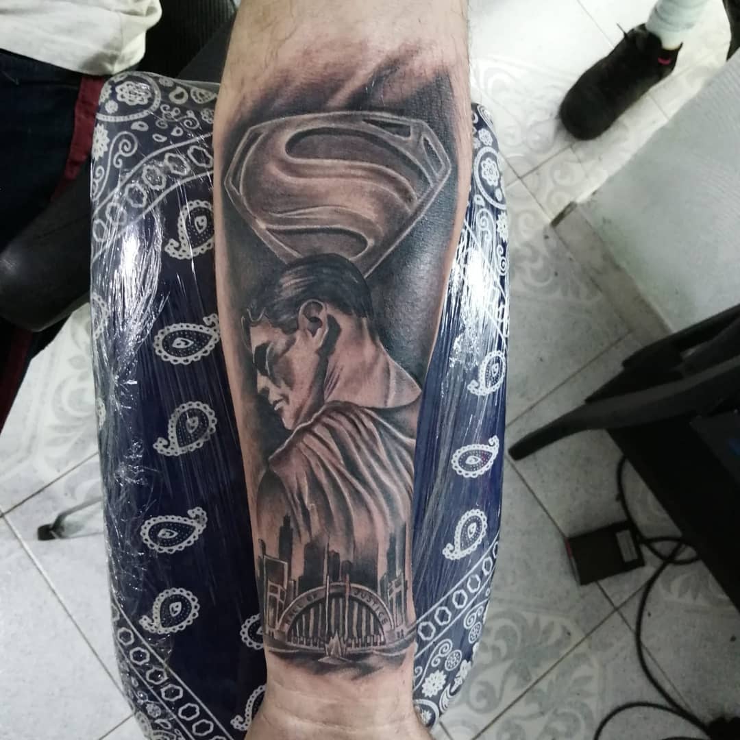 Tattoo of Superman above a cityscape on a forearm