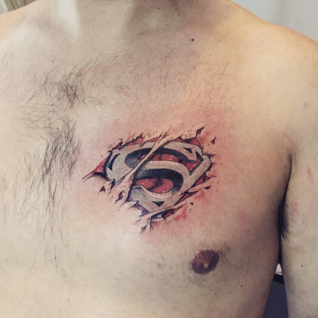 A man's chest with a tattoo of torn skin revealing the Superman logo beneath