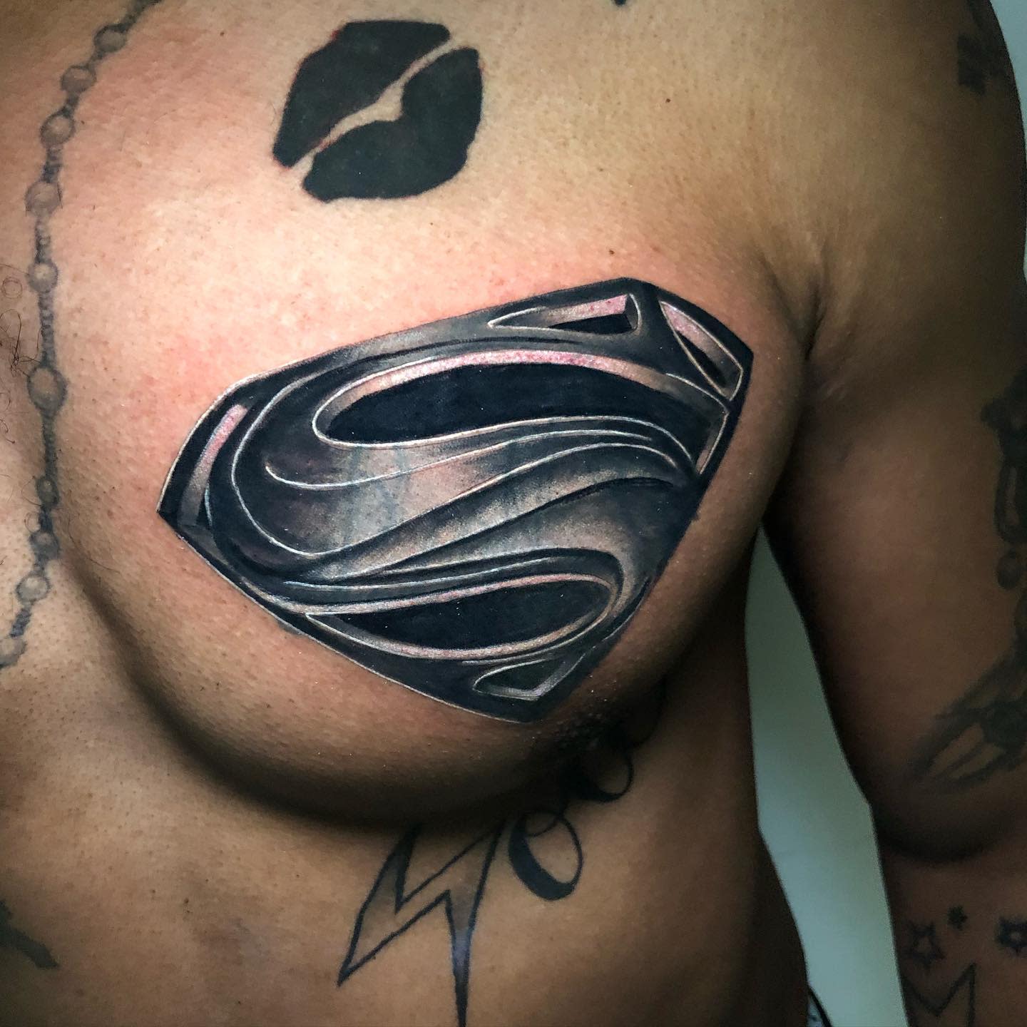Close-up of a chest tattoo featuring a black Superman emblem with surrounding tattoos