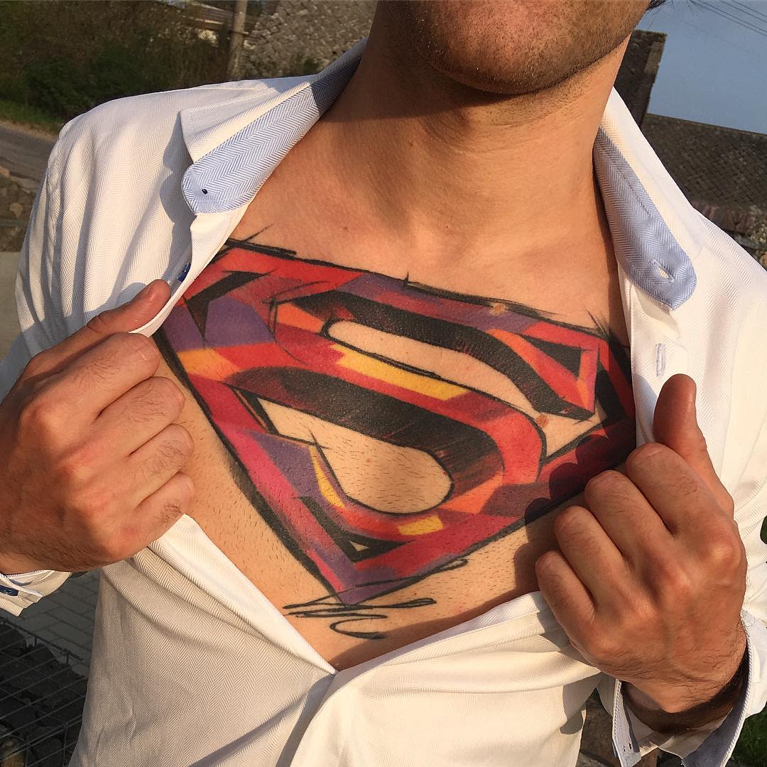A man pulls open his shirt to reveal a colorful Superman chest tattoo