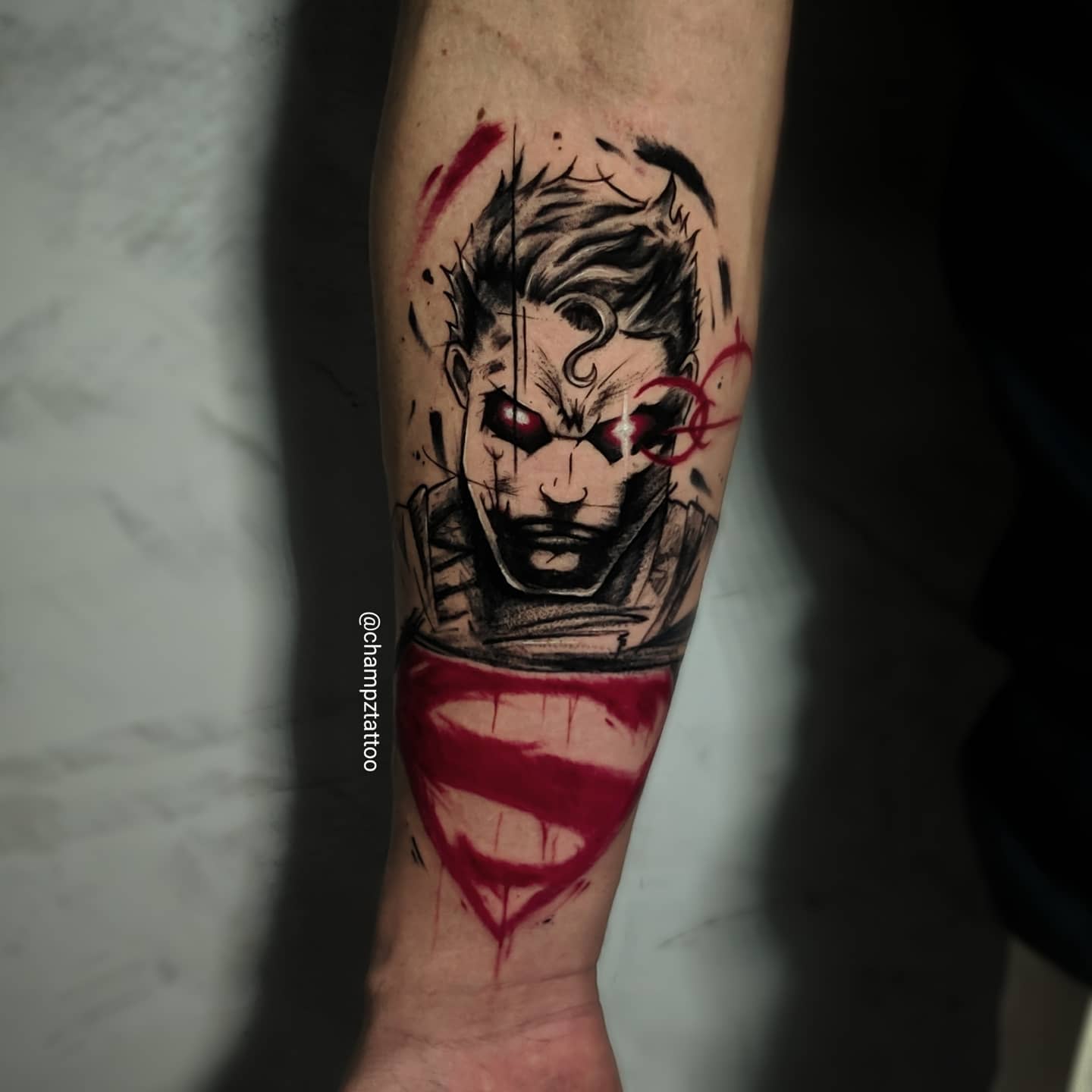 Forearm tattoo featuring a stylized, bloodied Superman with black and red ink