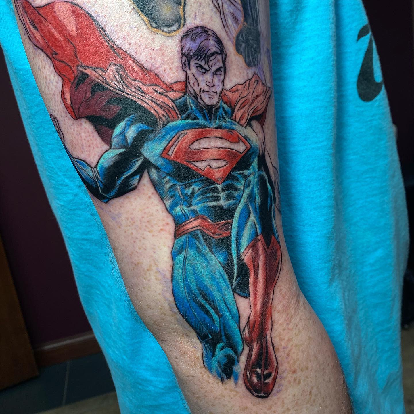 Colorful Superman tattoo showing him in flight with a red cape on an arm