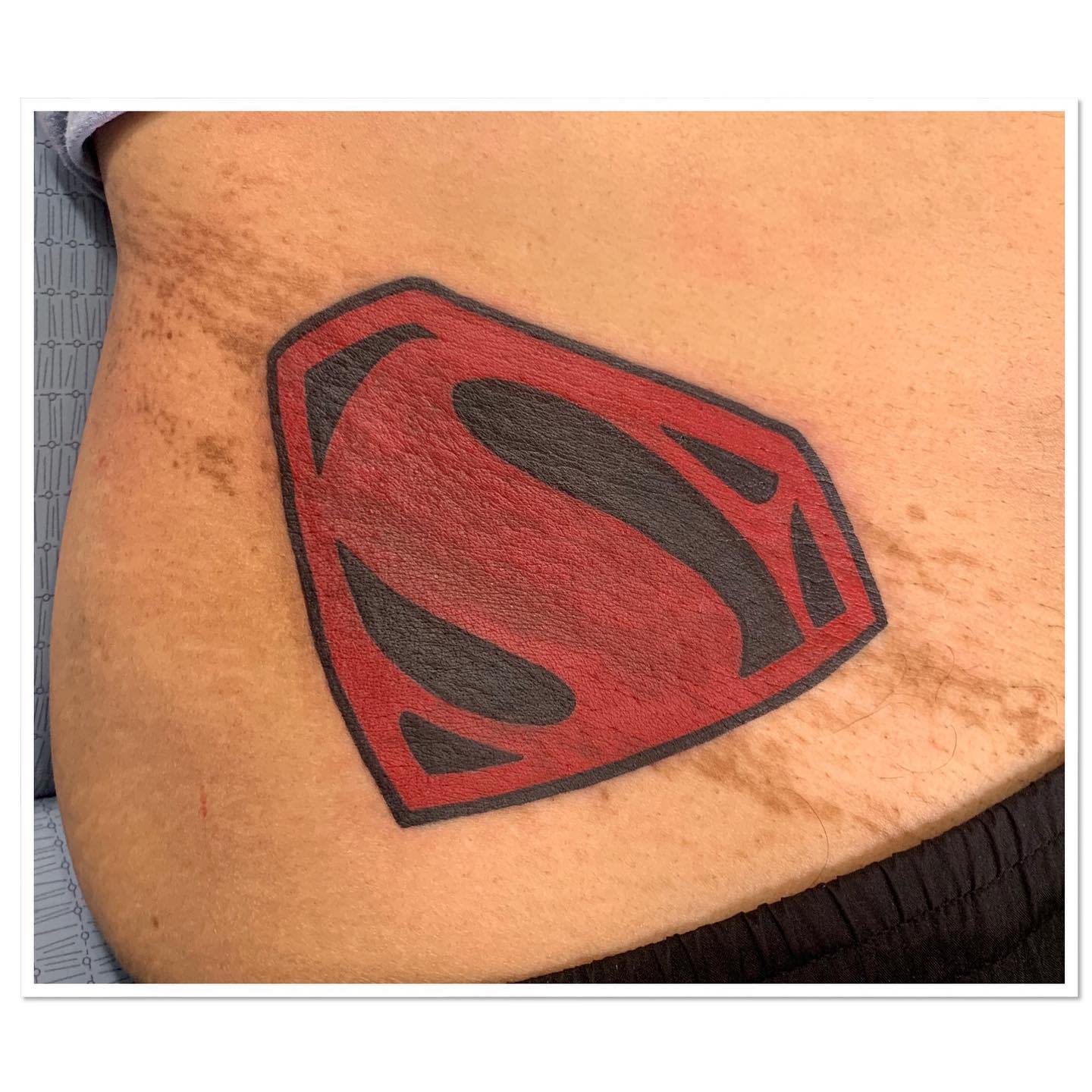 Red and black Superman logo tattoo on the left side of an individual's lower back