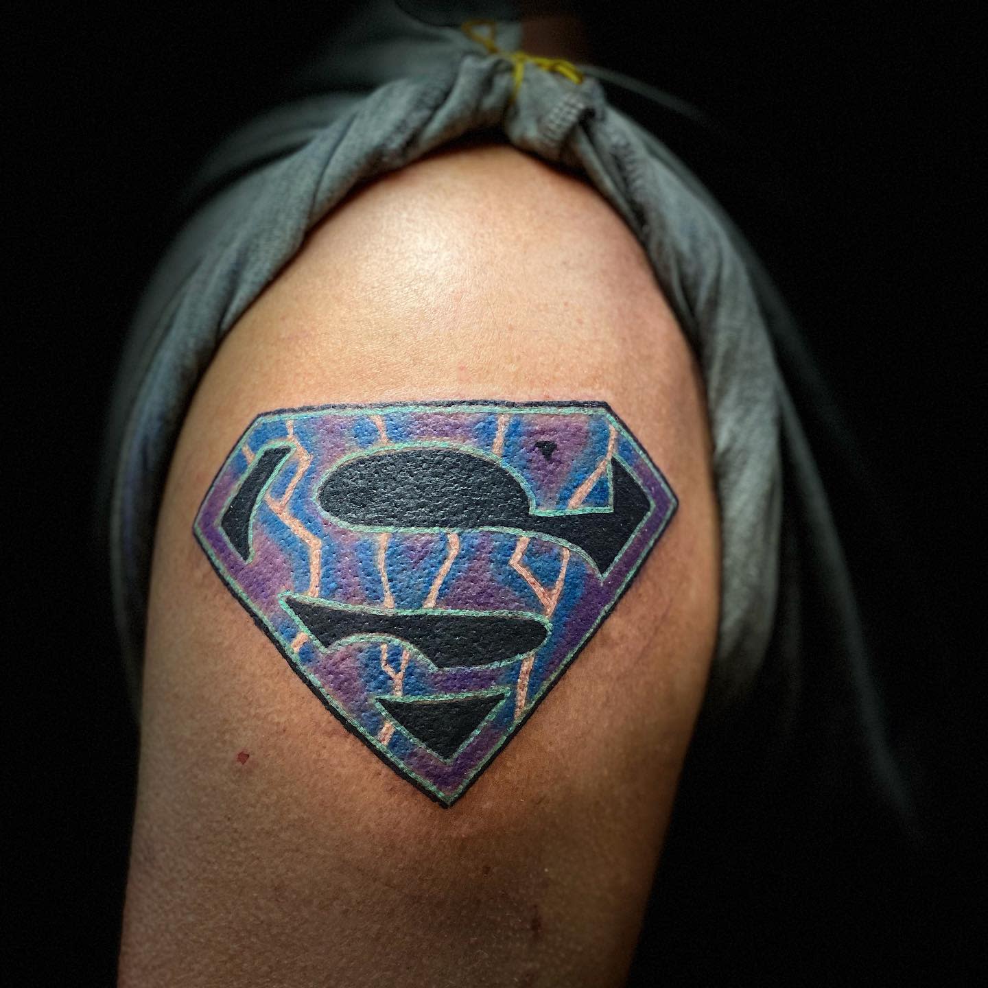 A colorful Superman logo tattoo on an upper arm