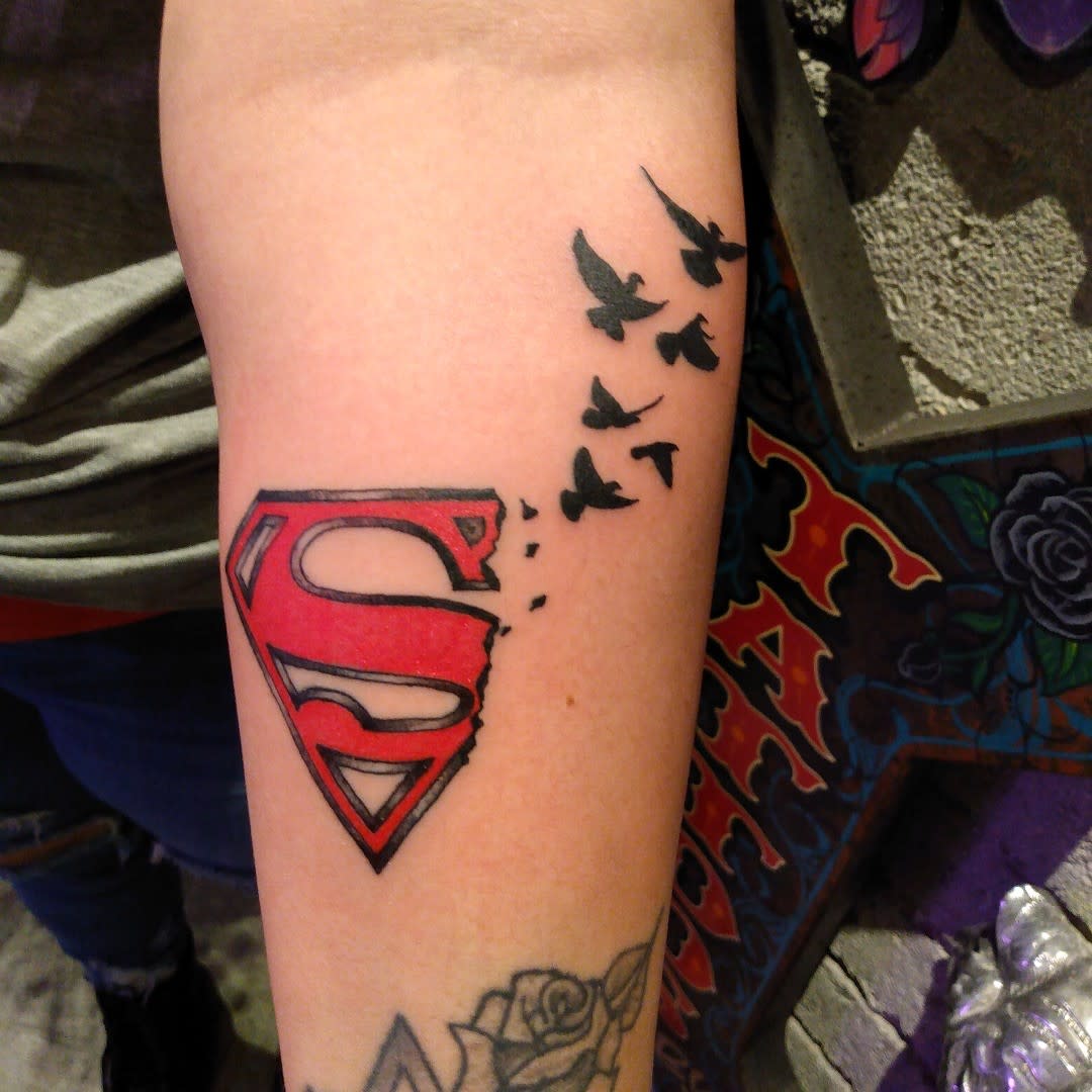 Superman logo tattoo with black birds flying away on a forearm