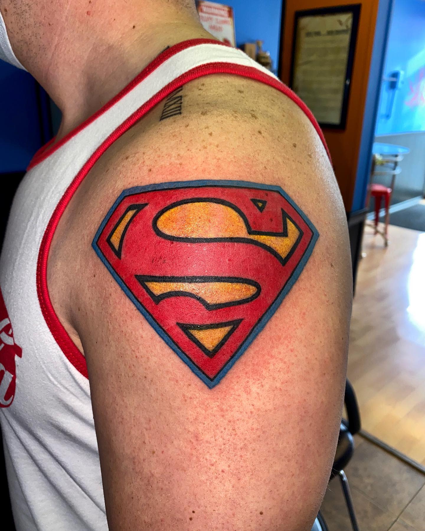 Close-up of a red and yellow Superman logo tattoo on an upper arm