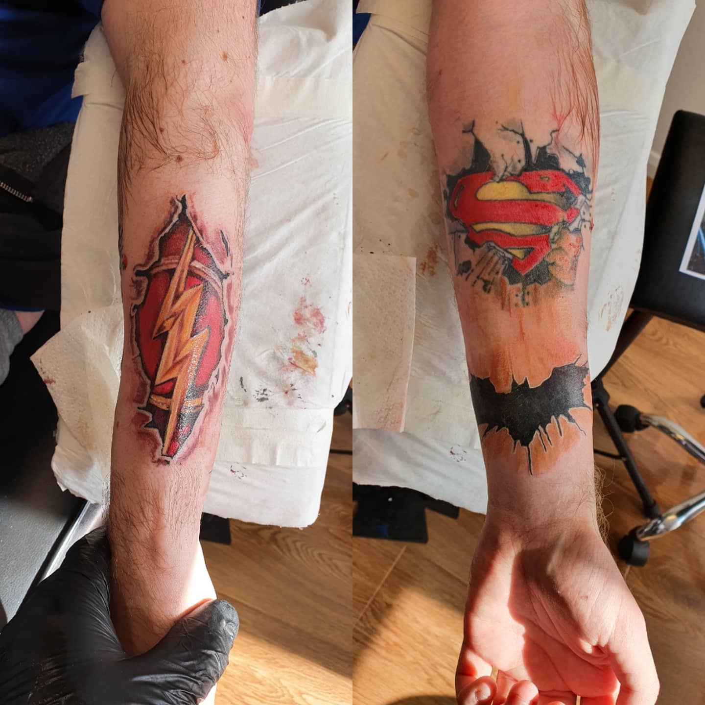Two forearms with fresh tattoos: Flash logo on left, Superman and Batman logos on right