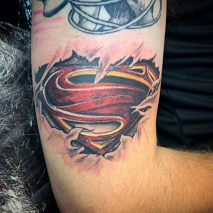 A tattoo of the Superman logo tearing through the skin on an arm