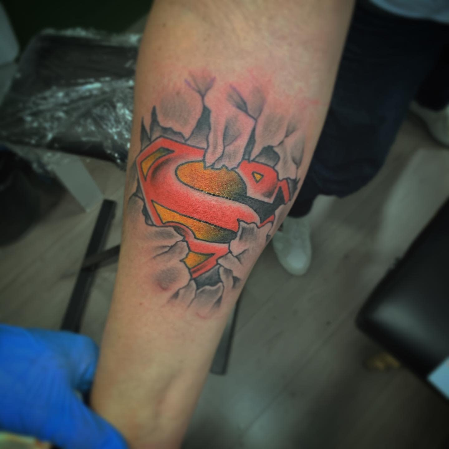 Arm tattoo of Superman logo appearing to rip through the skin