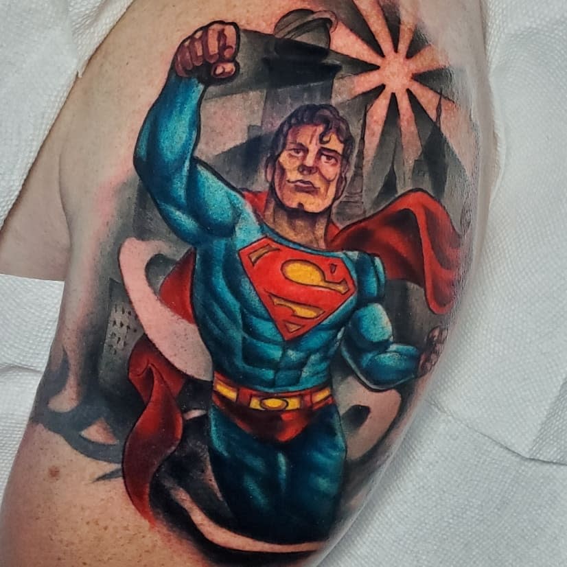 Tattoo of Superman in flight on an upper arm with a cityscape background