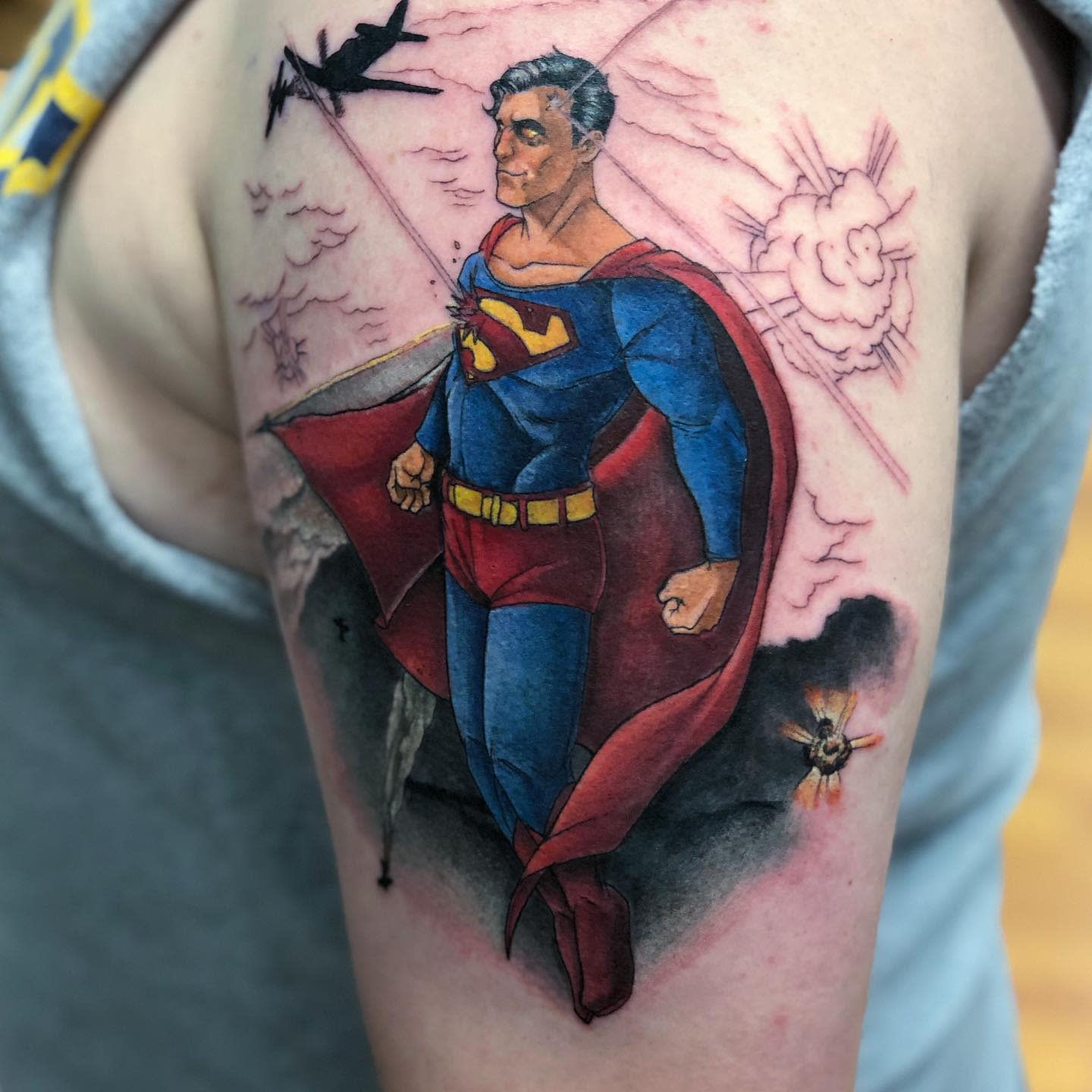 Colorful Superman tattoo with a dramatic background featuring planes and explosions