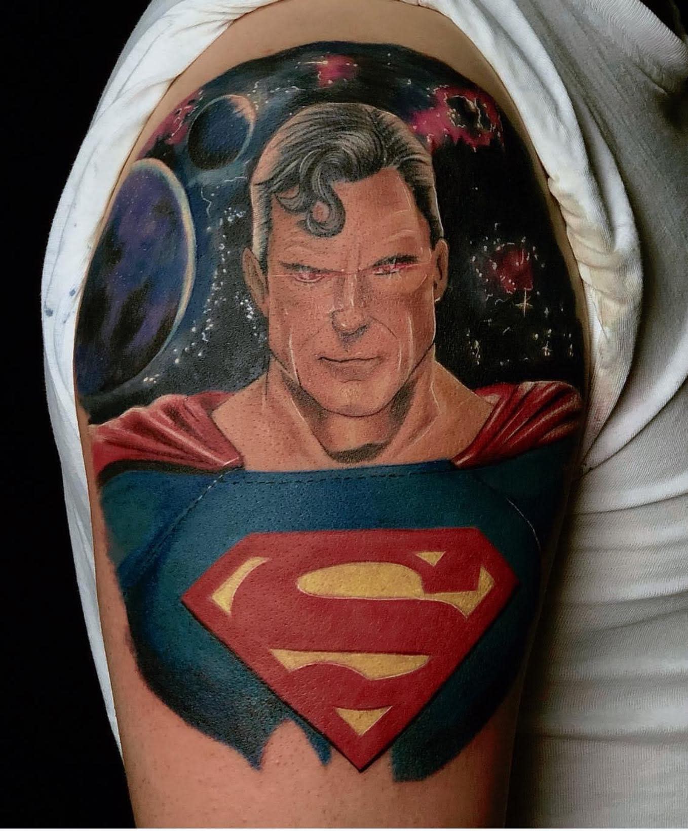 A tattoo of a comic-style superhero with planets in the background on an upper arm