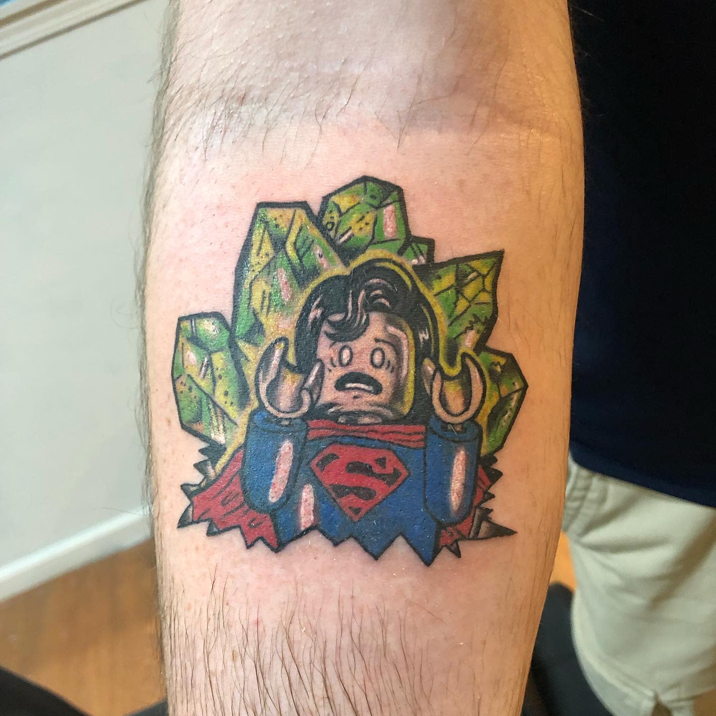 Tattoo of a Lego Superman breaking through kryptonite on a forearm