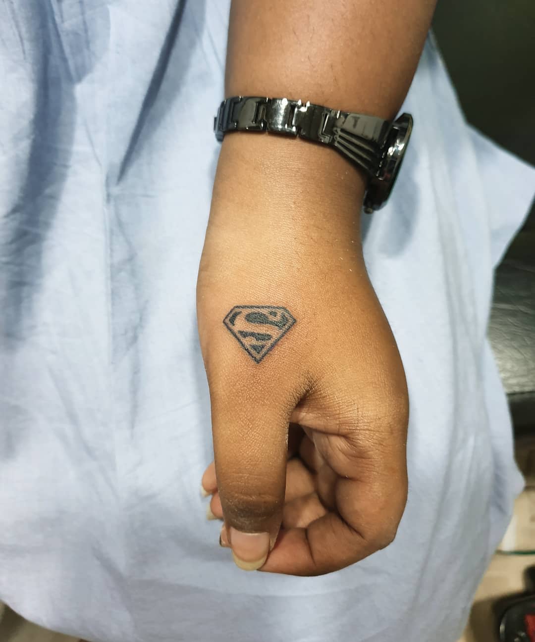 Wrist with a small Superman logo tattoo near the thumb