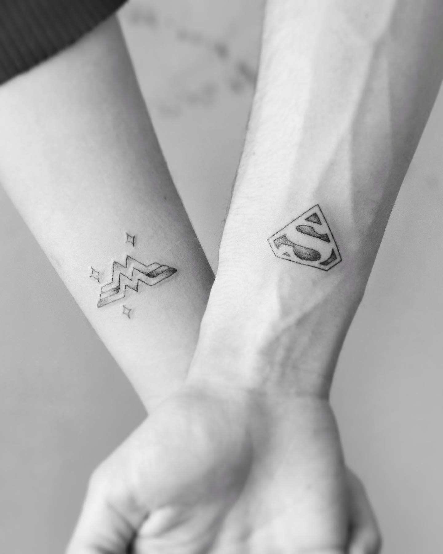 Two forearms with matching tattoos, arms intertwined One tattoo is a lightning bolt; the other, an S shield