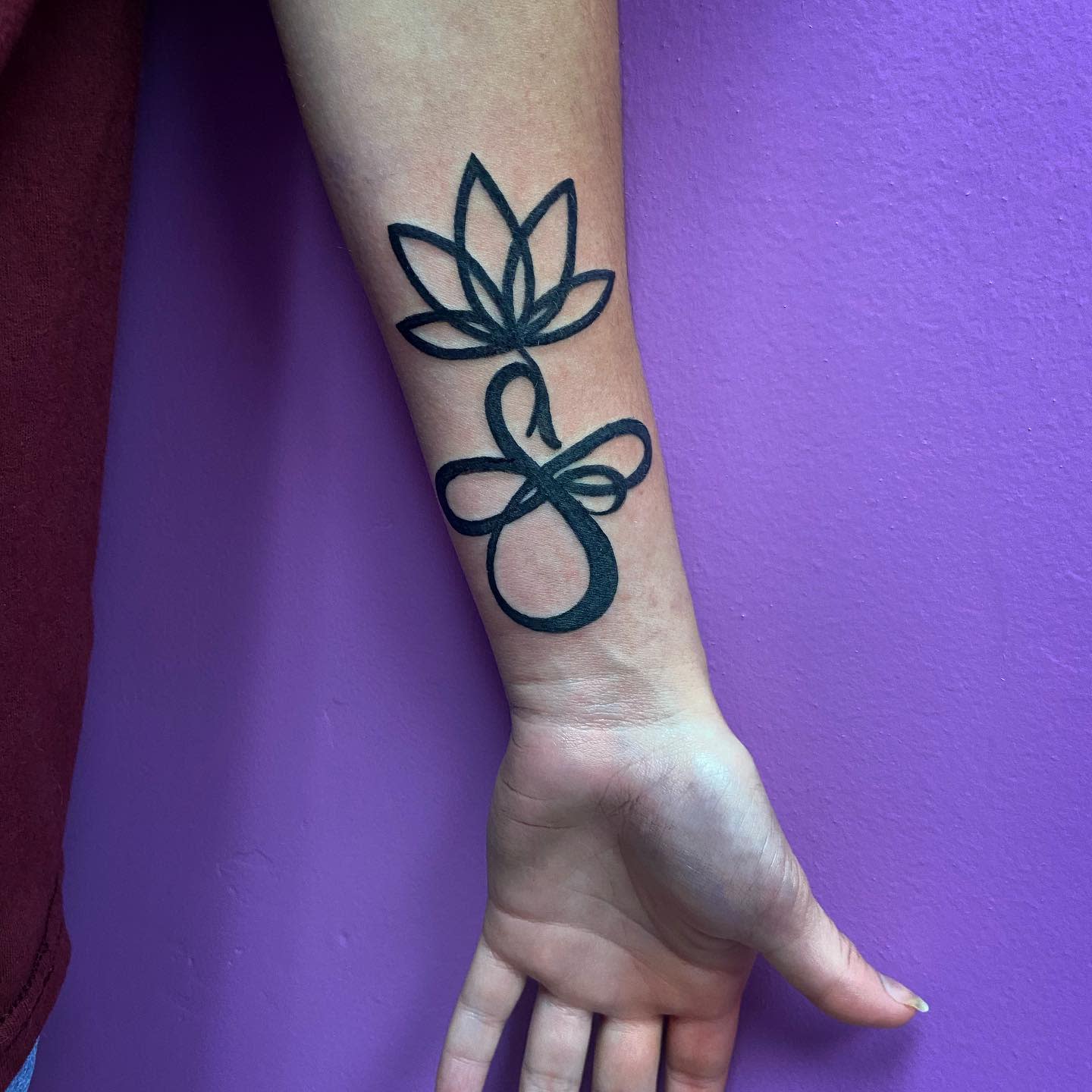 Forearm tattoo with a lotus flower and a cursive infinity symbol