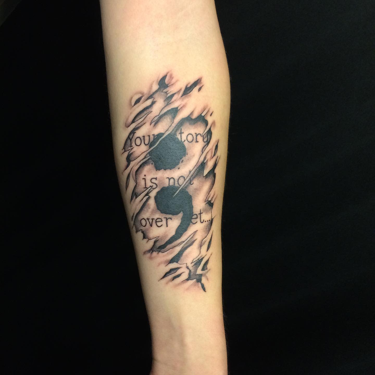 Forearm tattoo with torn skin effect and text "your story is not over yet"