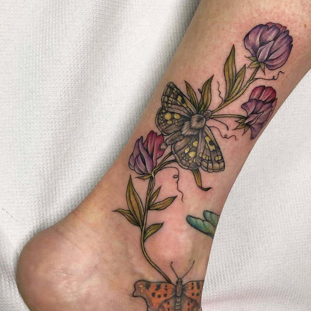 A delicate tattoo of sweet pea flowers with two moths, beautifully wrapped around the ankle