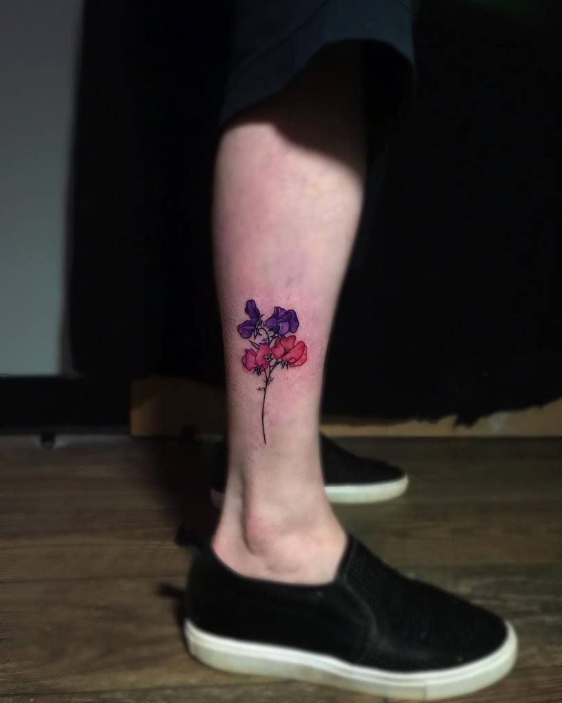 A colorful sweet pea flower tattoo featuring bold purple and pink petals, positioned on the ankle