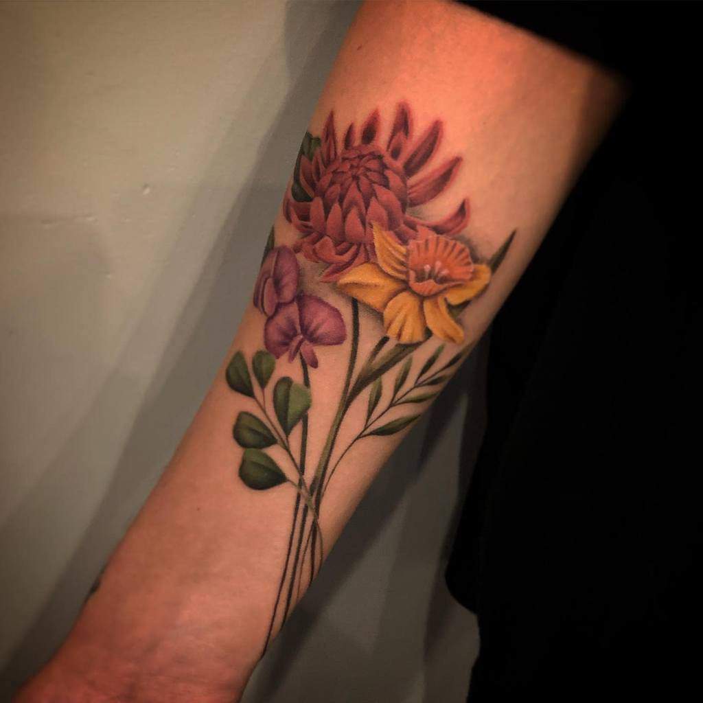 A vibrant forearm tattoo featuring sweet pea flowers, daffodils, and a large protea in bold colors