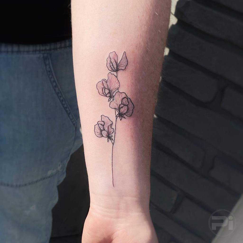 A delicate forearm tattoo featuring finely detailed sweet pea flowers in soft, subtle shading