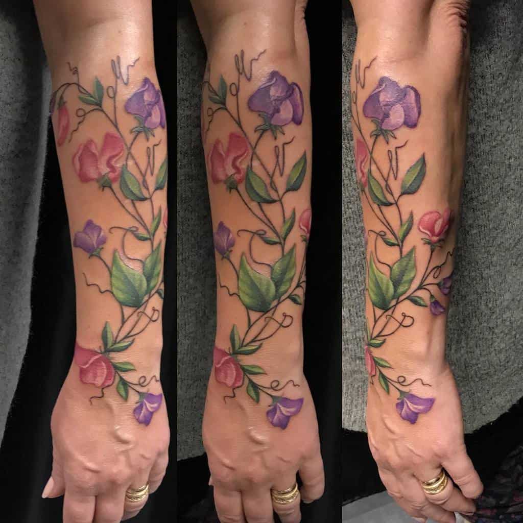 A vibrant full-forearm tattoo featuring pink and purple sweet pea flowers intertwined with green leaves