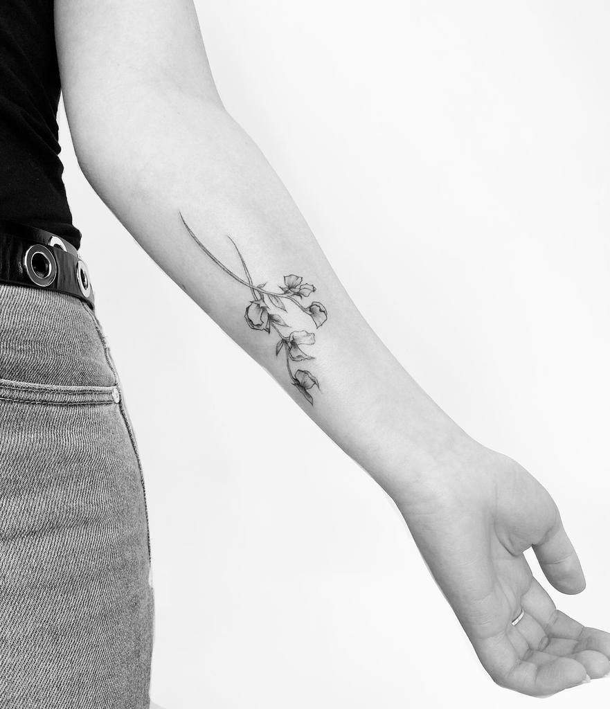 A delicate forearm tattoo featuring fine-line sweet pea flowers, elegantly placed along the arm