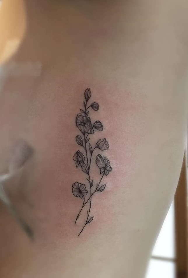 A fine-line sweet pea tattoo placed delicately on the ribs, featuring soft floral details