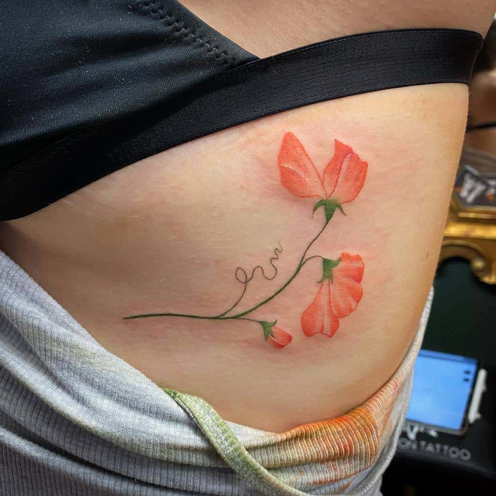 A vibrant rib tattoo featuring bright orange sweet pea flowers with delicate, flowing stems