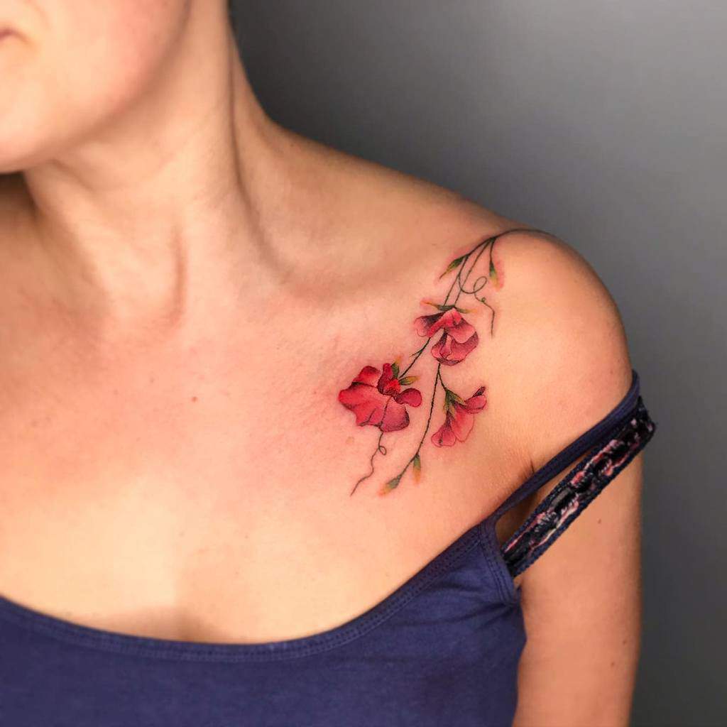 A delicate shoulder tattoo featuring bold sweet pea flowers in shades of pink and red, elegantly flowing down the collarbone