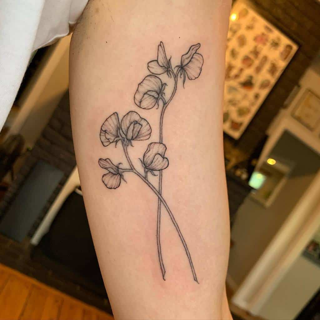 A simple and delicate sweet pea flower tattoo on the upper arm, featuring fine line work and minimalist details