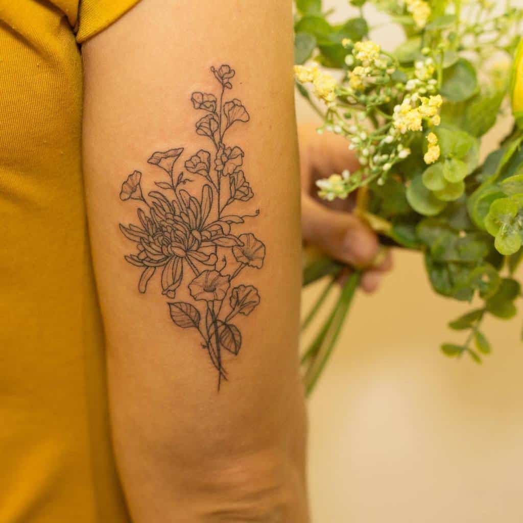 Sweet pea flower tattoo with detailed line art on the upper arm, combined with a chrysanthemum